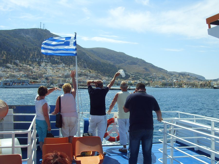 Passagiere grüßen von einer Fähre vor der Küste von Kalymnos.