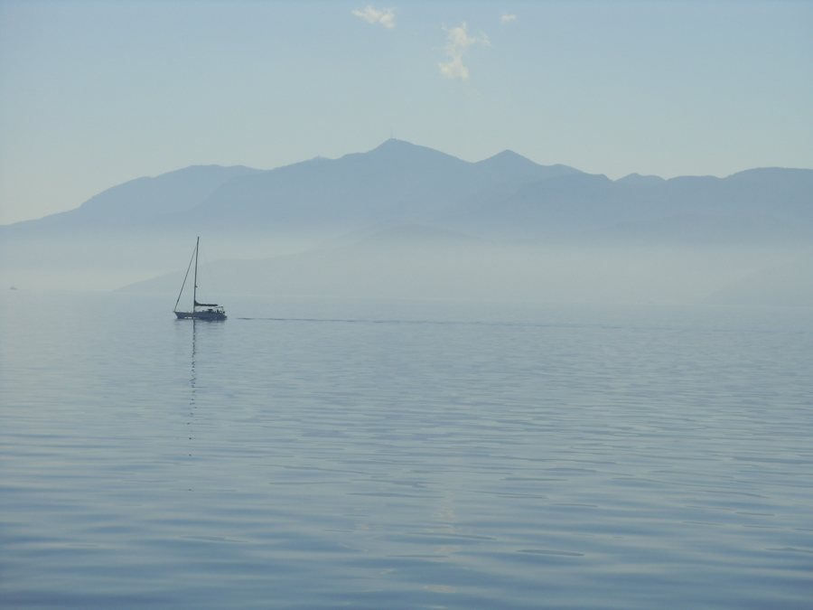 Segelboot auf ruhigem Wasser vor einer fernen Bergküste