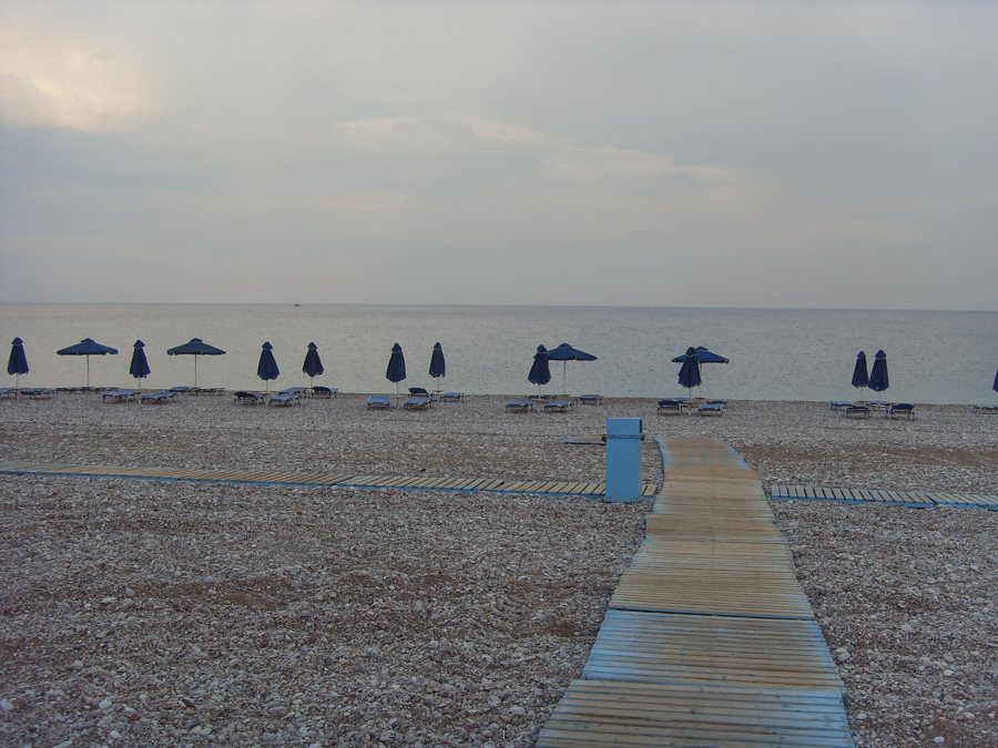 Holzsteg führt über einen Kiesstrand bis zum Wasser.